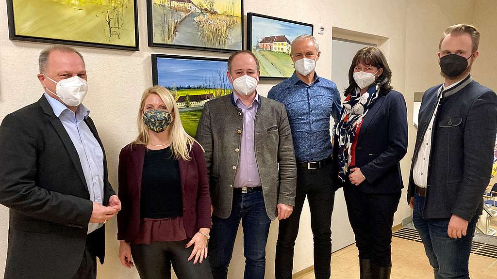 6 Personen, alle Masken tragend, vor einer Wand mit Bildern