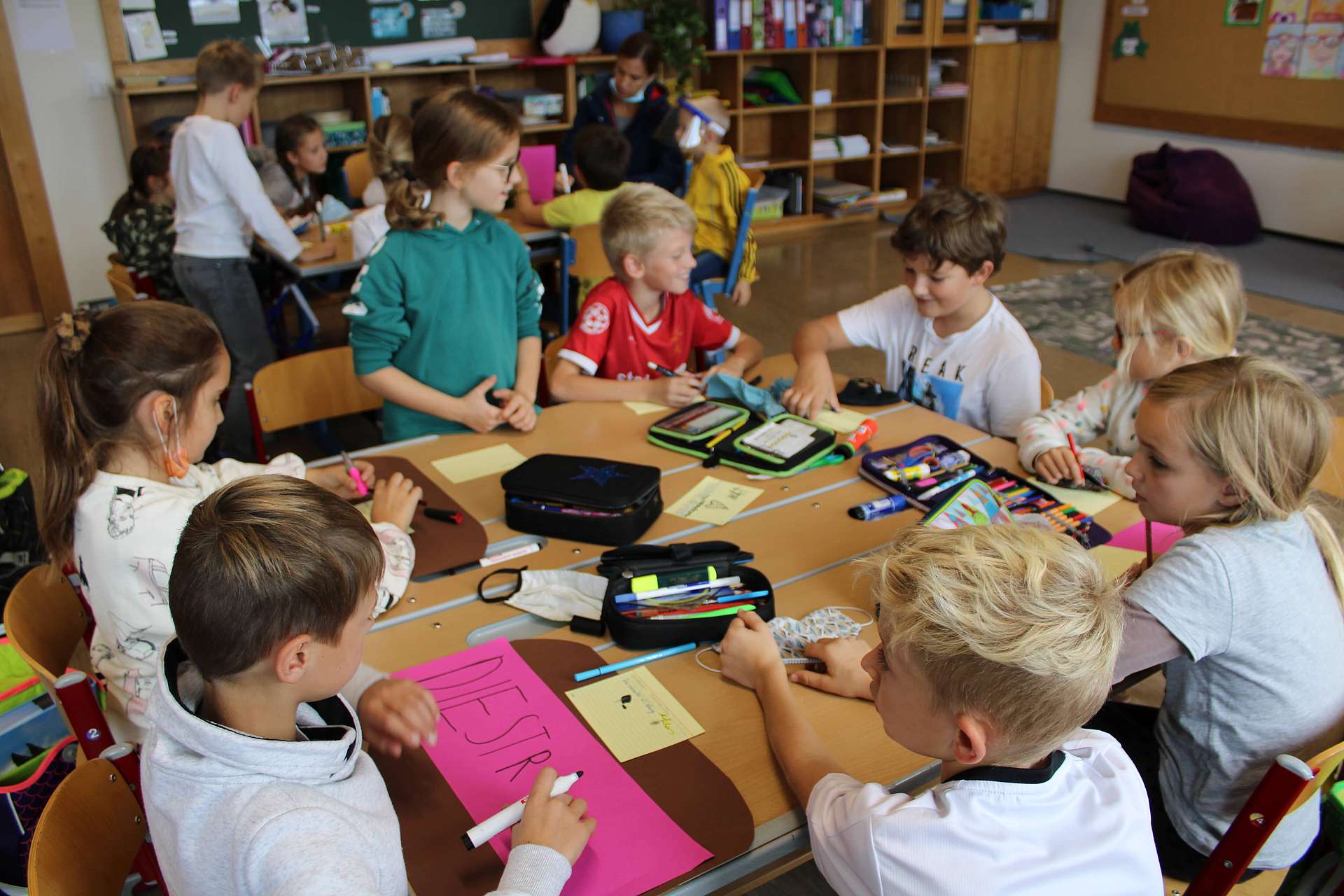 Zehn Kinder sitzen in einer Schulklasse arbeitend und lachend an einem Tische