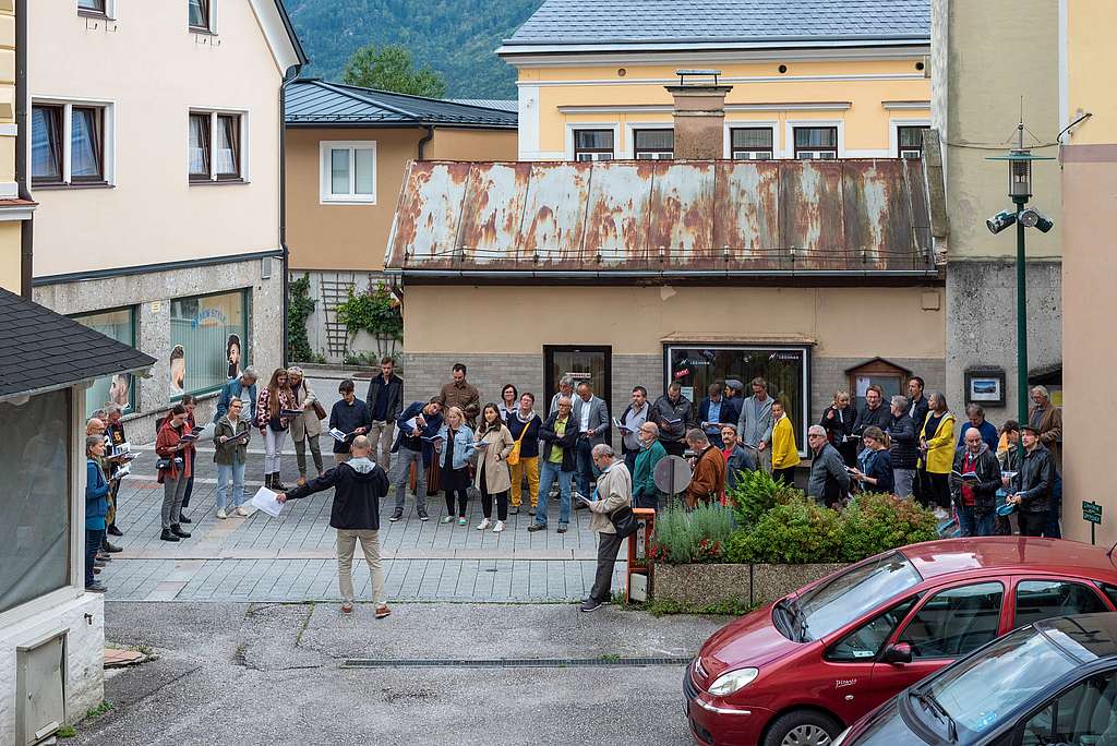 Ca. 30 Personen auf einer Straße vor einem baufälligen Gebäude