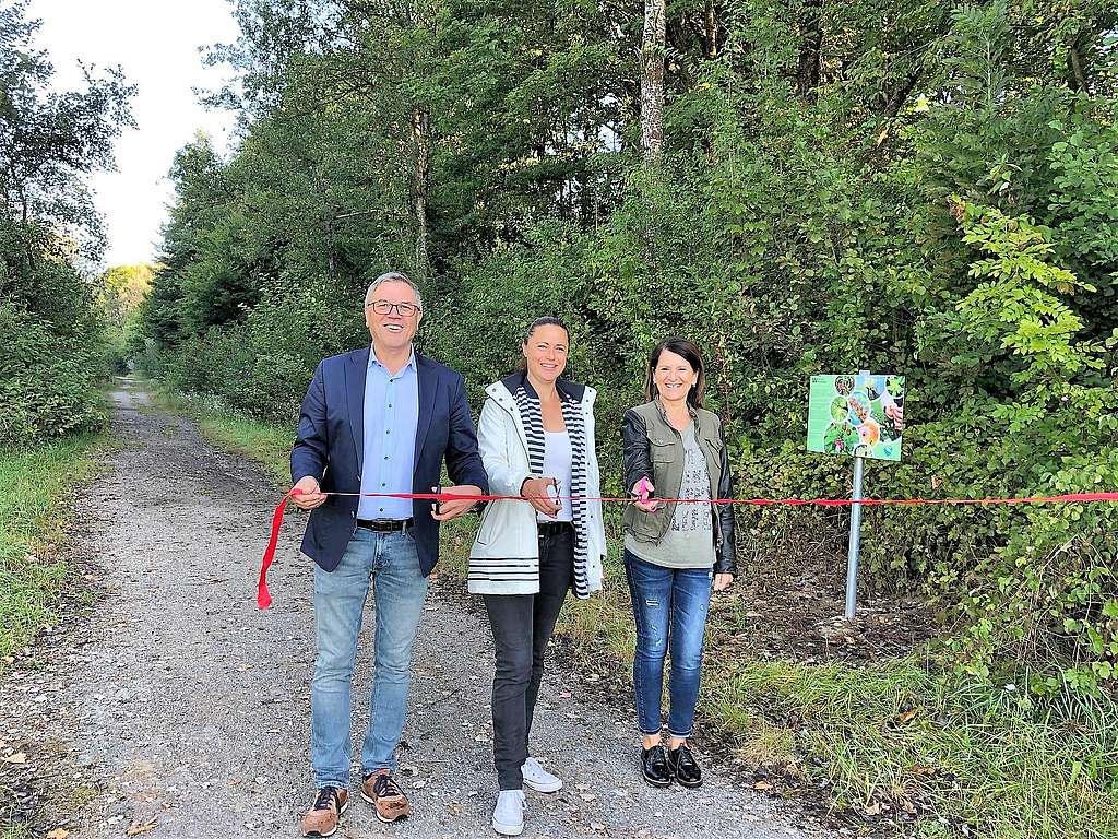 Ein Mann und zwei Frauen auf einem Schotterweg im Wald schneiden das rote Eröffnungsband durch
